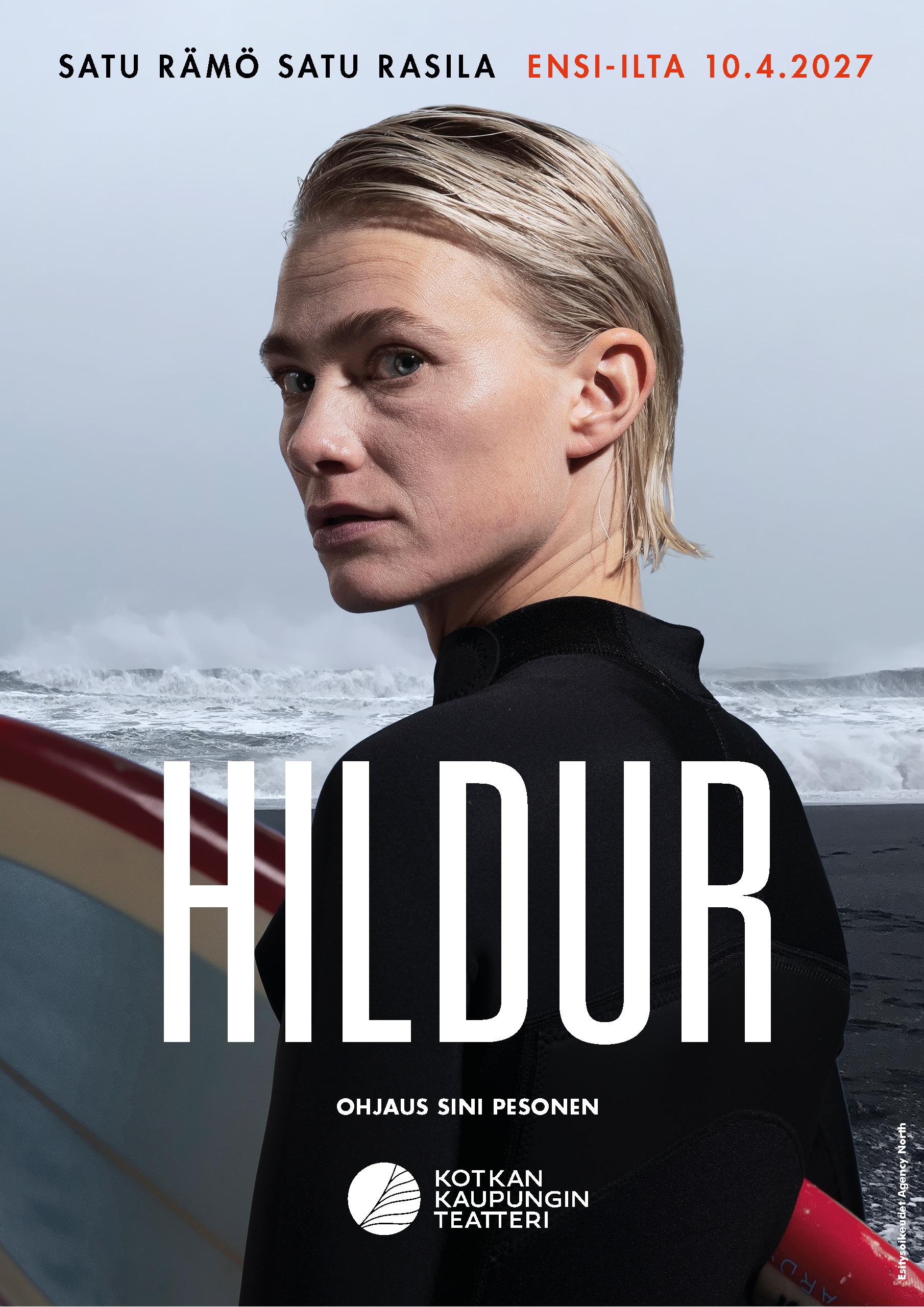 Hildur-esityksen juliste. Märkäpukuun pukeutunut näyttelijä seisoo meren rannalla surffilauta kädessään ja katsoo olkansa yli kohti kameraa. Taustalla näkyy aallokko ja harmaa taivas. Julisteessa lukee Hildur, ensi-ilta 10.4.2027, ohjaus Sini Pesonen sekä Kotkan Kaupunginteatterin logo.